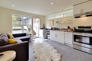 A modern kitchen with stainless steel appliances, a dining area with a sofa and a rug, and large windows offering a view of the outdoors.