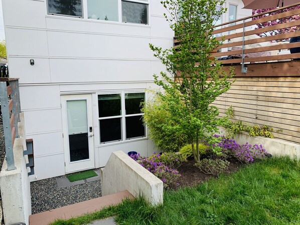 A white two-story house with a small garden, a wooden fence, and a door with a window.
