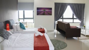 Ett modernt hotellrum med två sängar, en soffa, en tavla och stora fönster med gardiner.