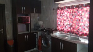 A compact kitchen with dark cabinets, a washing machine, and a sink under a polka dot curtain. - mmmHouse Abuja (Abuja)