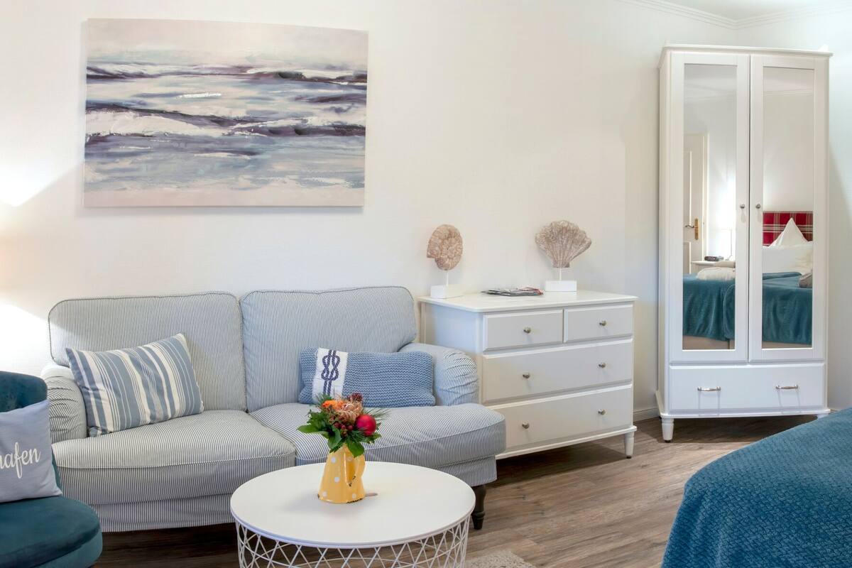 A modern bedroom with a striped sofa, a round coffee table with a vase, a wardrobe, and a painting on the wall.