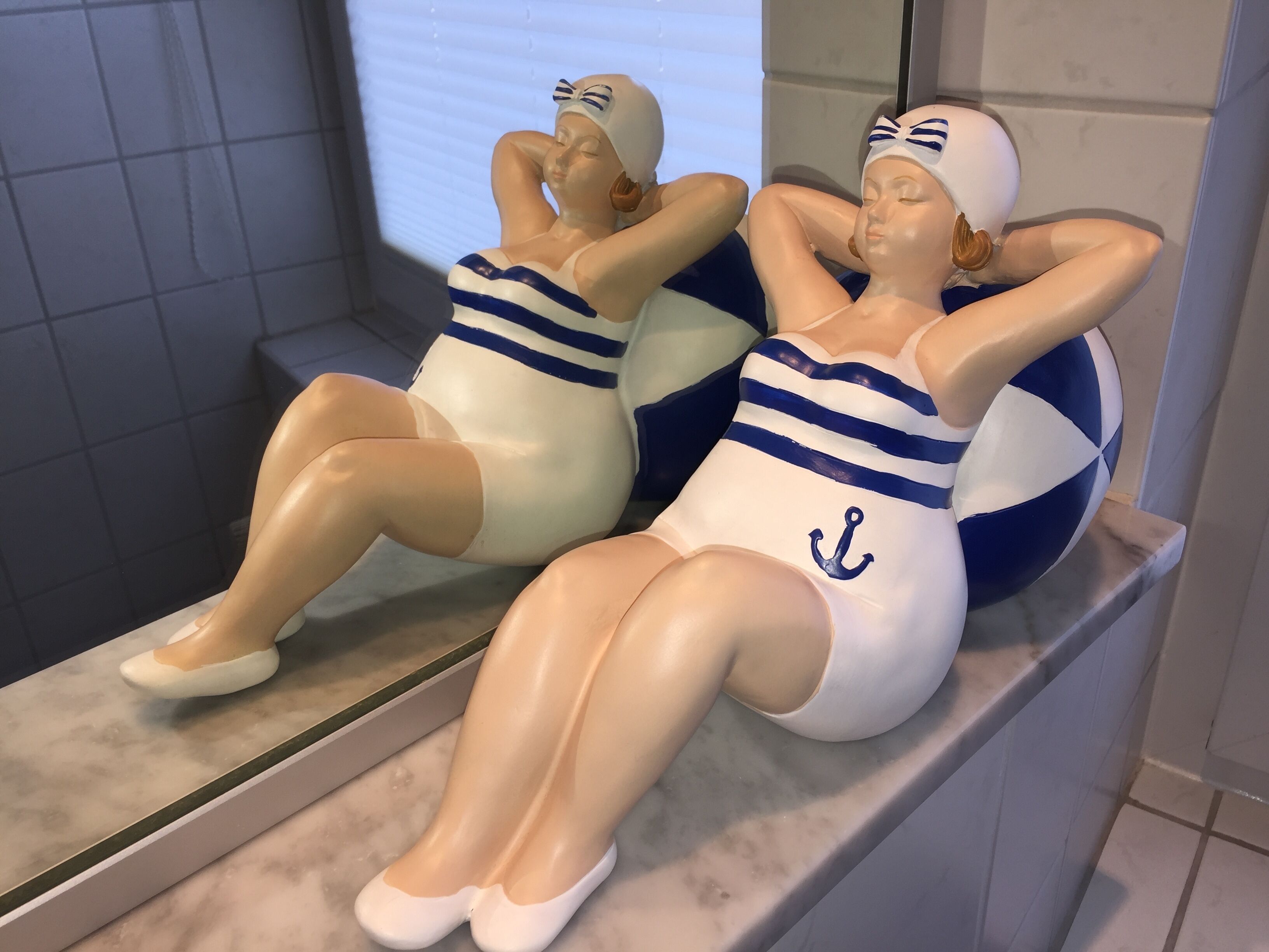 Two statues of women in swimwear sitting on a marble ledge.