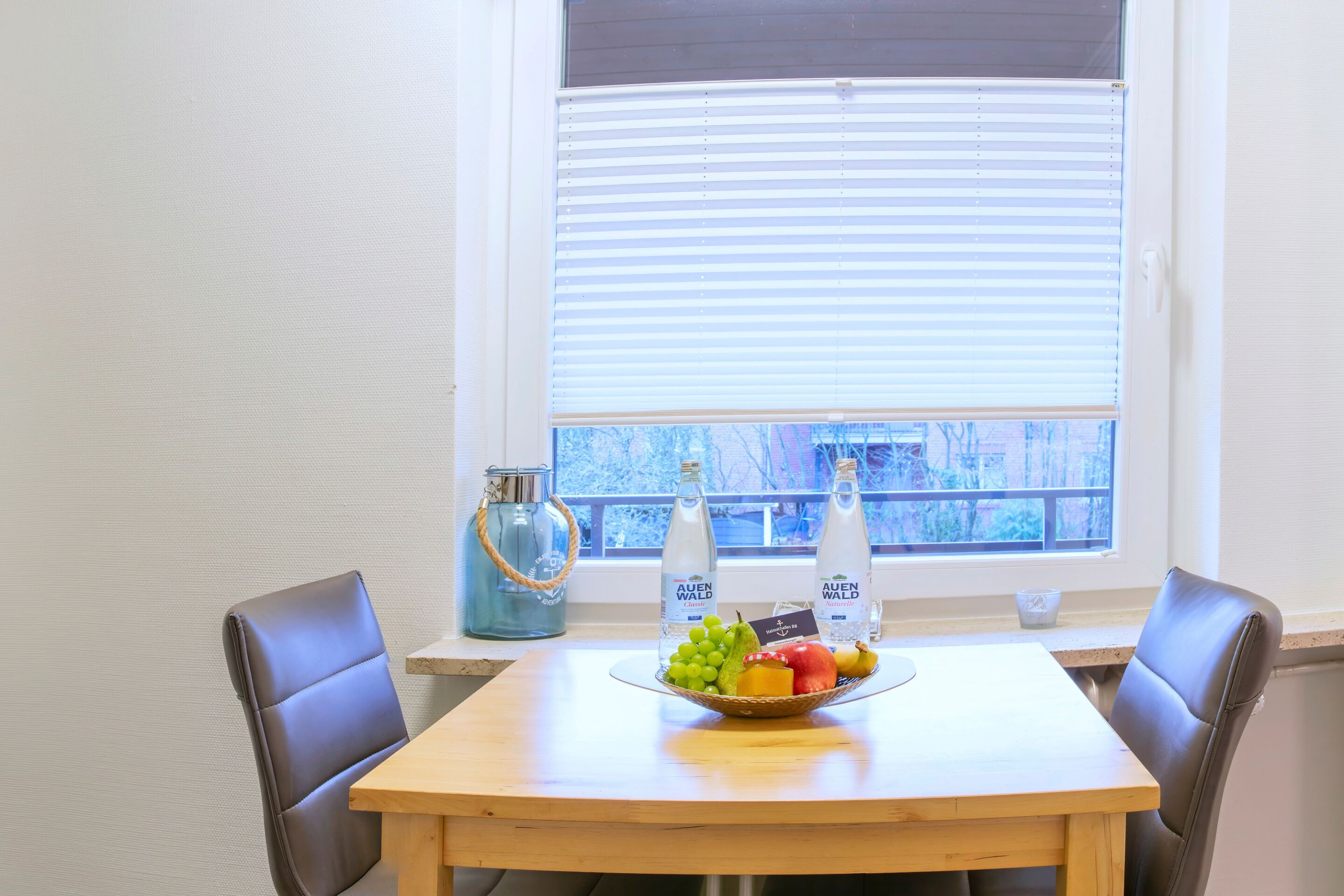 A dining area with a table, chairs, a fruit bowl, and two bottles of water.