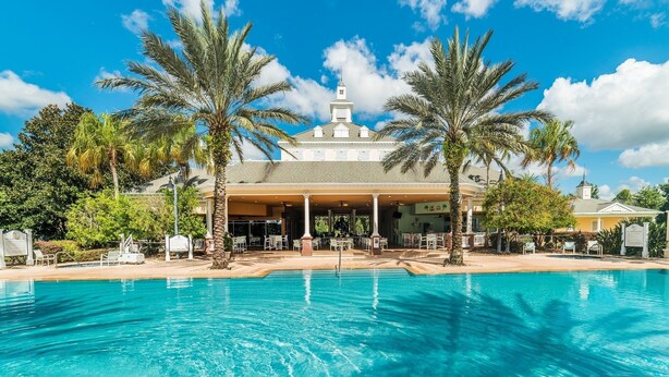A hotel with a swimming pool, palm trees, and a covered outdoor area with seating.