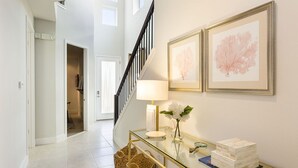 A modern interior with a glass console table, a staircase, and framed artwork on the wall.
