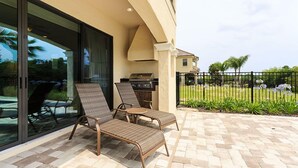 Un patio con dos sillones, una parrilla y una puerta de vidrio que da a una piscina.