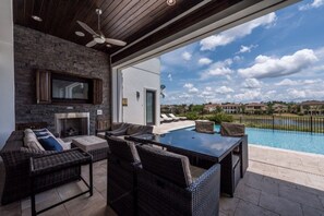 Une terrasse extérieure avec des meubles en osier, une cheminée en pierre et une vue sur la piscine.