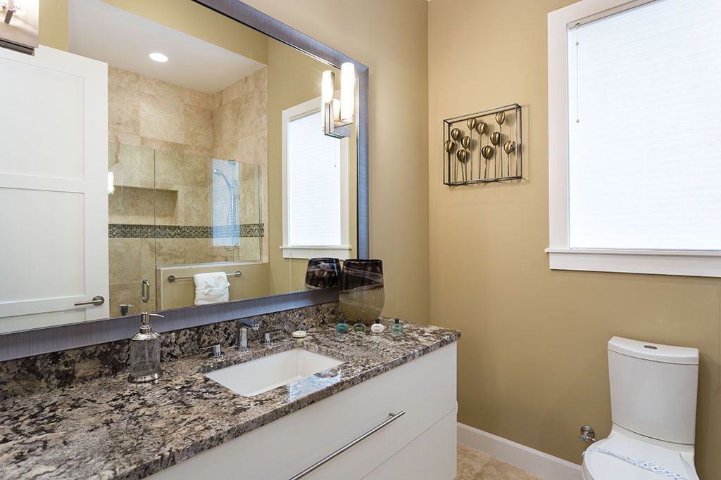 A bathroom with a granite countertop, a large mirror, a toilet, and a decorative wall piece.