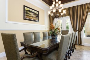 Une salle à manger avec une table à plateau de verre entourée de chaises rembourrées, un lustre et un tableau représentant un paysage, accroché au mur.