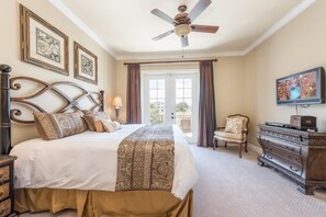 Une chambre à coucher avec un grand lit, un ventilateur de plafond, une commode, une chaise et un téléviseur.