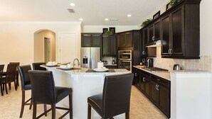 Une cuisine moderne avec des meubles de rangement aux couleurs sombres, un îlot central doté de tabourets et des appareils électroménagers intégrés.