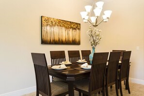 Un comedor con una mesa y sillas de madera oscura, un jarrón con flores y un cuadro en la pared.