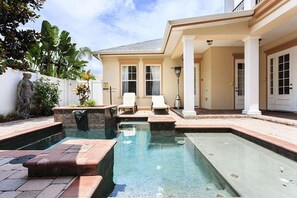 A swimming pool area with two lounge chairs, a statue, and a covered patio.