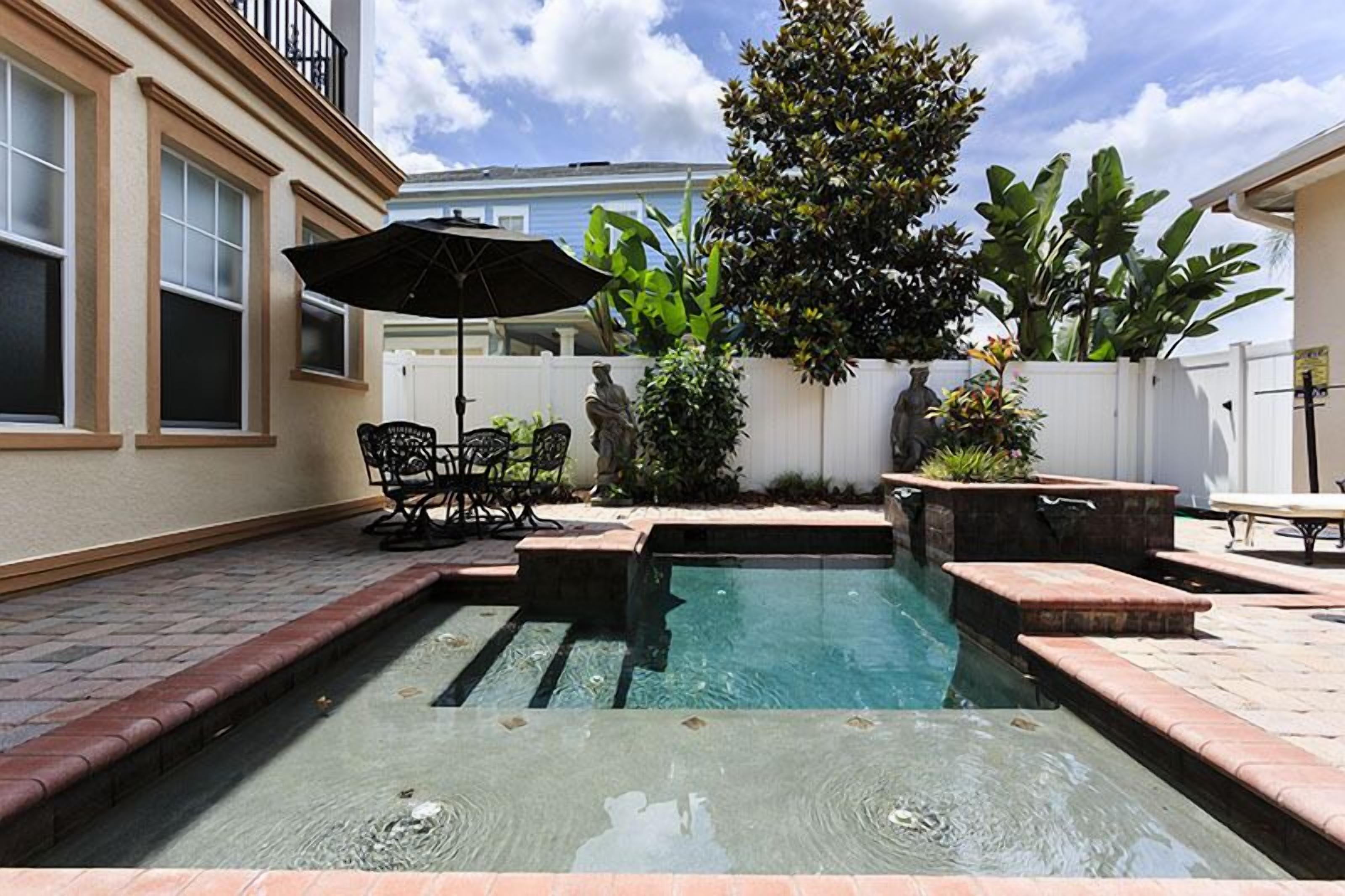 A backyard with a swimming pool, patio furniture, and a white fence.