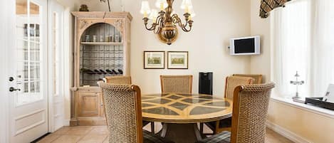 Un comedor con una mesa redonda, cuatro sillas de mimbre, una araña, una vinoteca y un televisor en la pared.