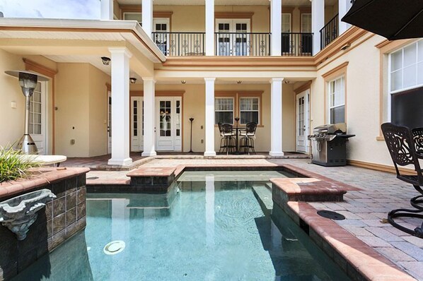 A pool area with a two-story building, a patio with outdoor furniture, and a covered seating area.