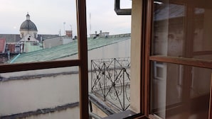 En vy genom ett fönster i en byggnad med ett metallräcke på balkongen, en kupolformad konstruktion i bakgrunden och ett grönt tak.