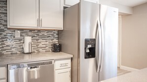 Eine moderne Küche mit weißen Schränken, einem Edelstahlkühlschrank, einer Spülmaschine und einer Kaffeemaschine auf der Arbeitsplatte.