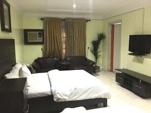A hotel room with a bed, a sofa, a TV, and a potted plant. - Sun On Hotel (Lagos)