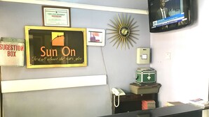 A reception area with a 'Sun On' sign, a suggestion box, a framed certificate, a clock, a television, and a telephone. - Sun On Hotel (Lagos)