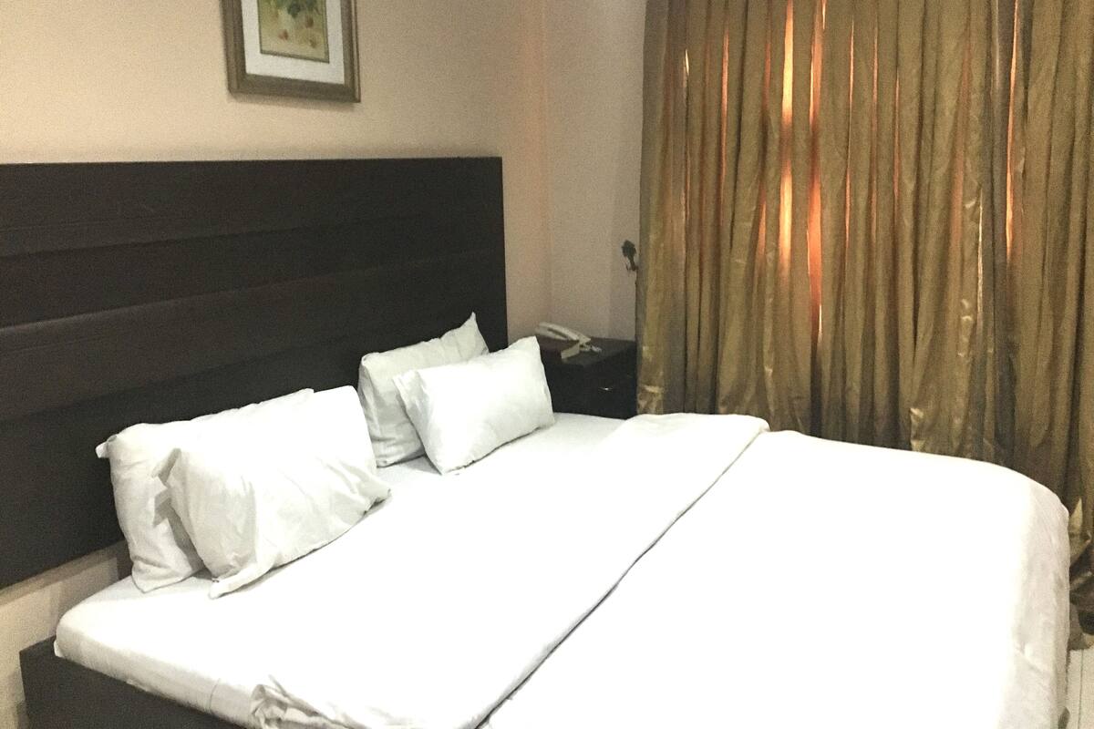 Hotellihuone, jossa on suuri sänky, valkoiset vuodevaatteet, tumma pääty, seinällä kehystetty taulu ja verho.