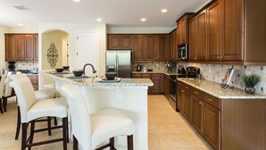 A modern kitchen with wooden cabinets, a central island with bar stools, and a stainless steel refrigerator. - Je58253 - Reunion Resort - 6 Bed 5 Baths Villa (Kissimmee)