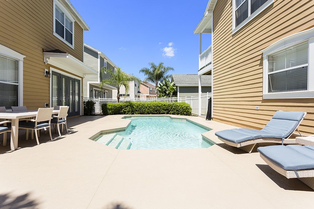 A backyard with a swimming pool, lounge chairs, a dining table, and a small patio area.