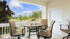 A balcony with a round table and four chairs, overlooking a golf course with palm trees. - Je58447 - Reunion Resort - 3 Bed 2 Baths Condo (Kissimmee)