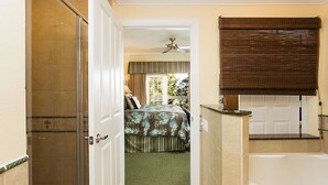A hotel room with a shower, a bed with a floral bedspread, a window with curtains, and a bathroom with a bathtub and a towel rack. - Je58447 - Reunion Resort - 3 Bed 2 Baths Condo (Kissimmee)
