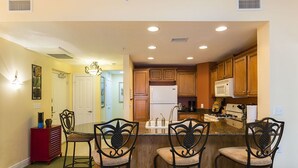 A kitchen with wooden cabinets, a refrigerator, a microwave, and a bar area with four chairs. - Je58447 - Reunion Resort - 3 Bed 2 Baths Condo (Kissimmee)