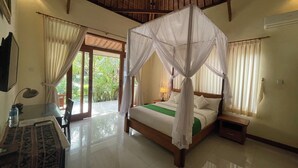 A bedroom with a canopy bed, a desk with a chair, and a view of the outdoors through a sliding door. - Graha Madesimon (Batubulan)