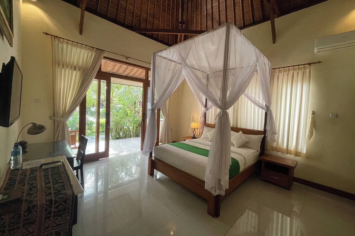 Quarto com cama de dossel, escrivaninha com cadeira e vista para o exterior por uma porta de correr.