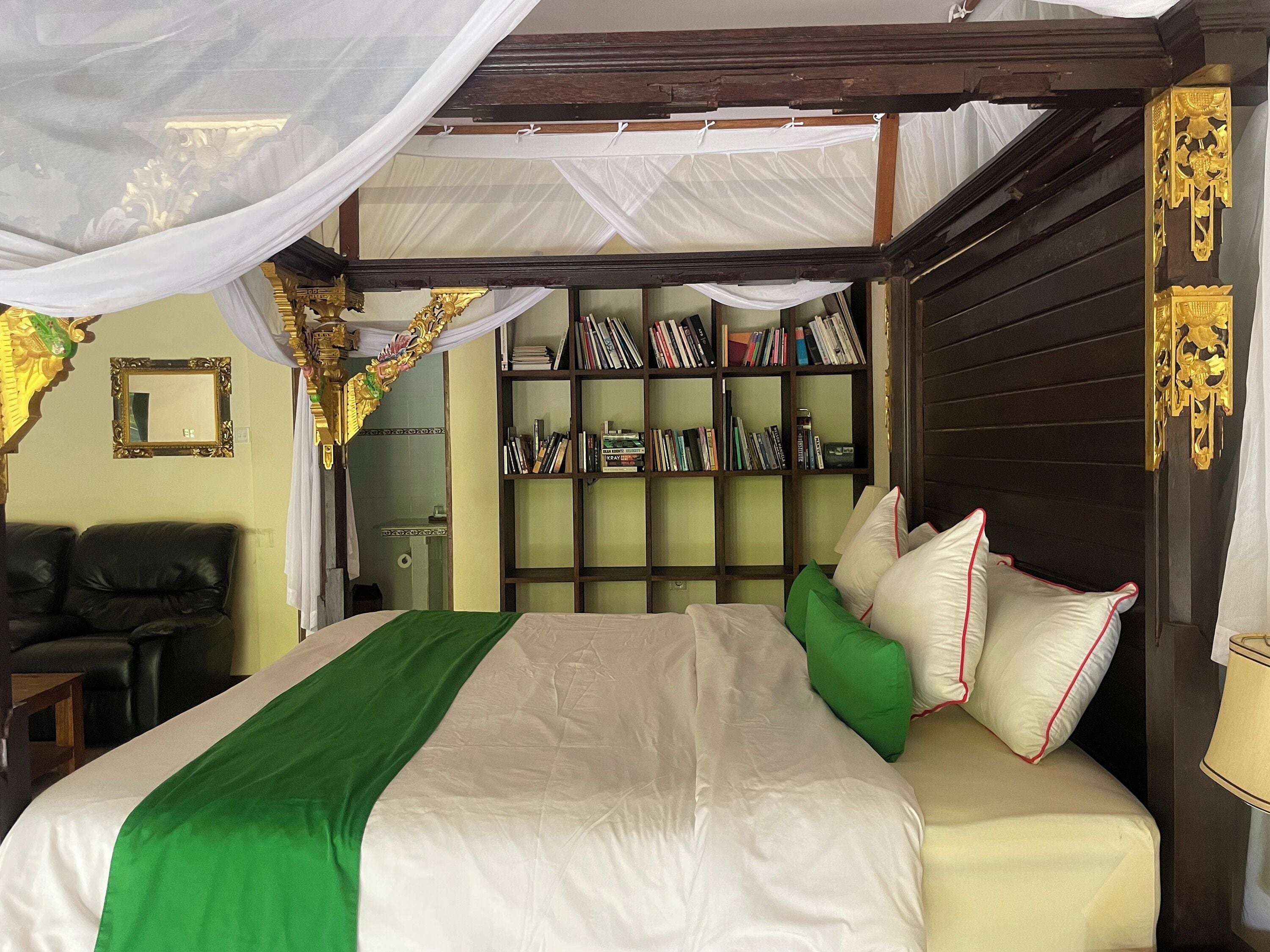 Ein Schlafzimmer mit einem Himmelbett, einem Bücherregal und einem Ledersessel.