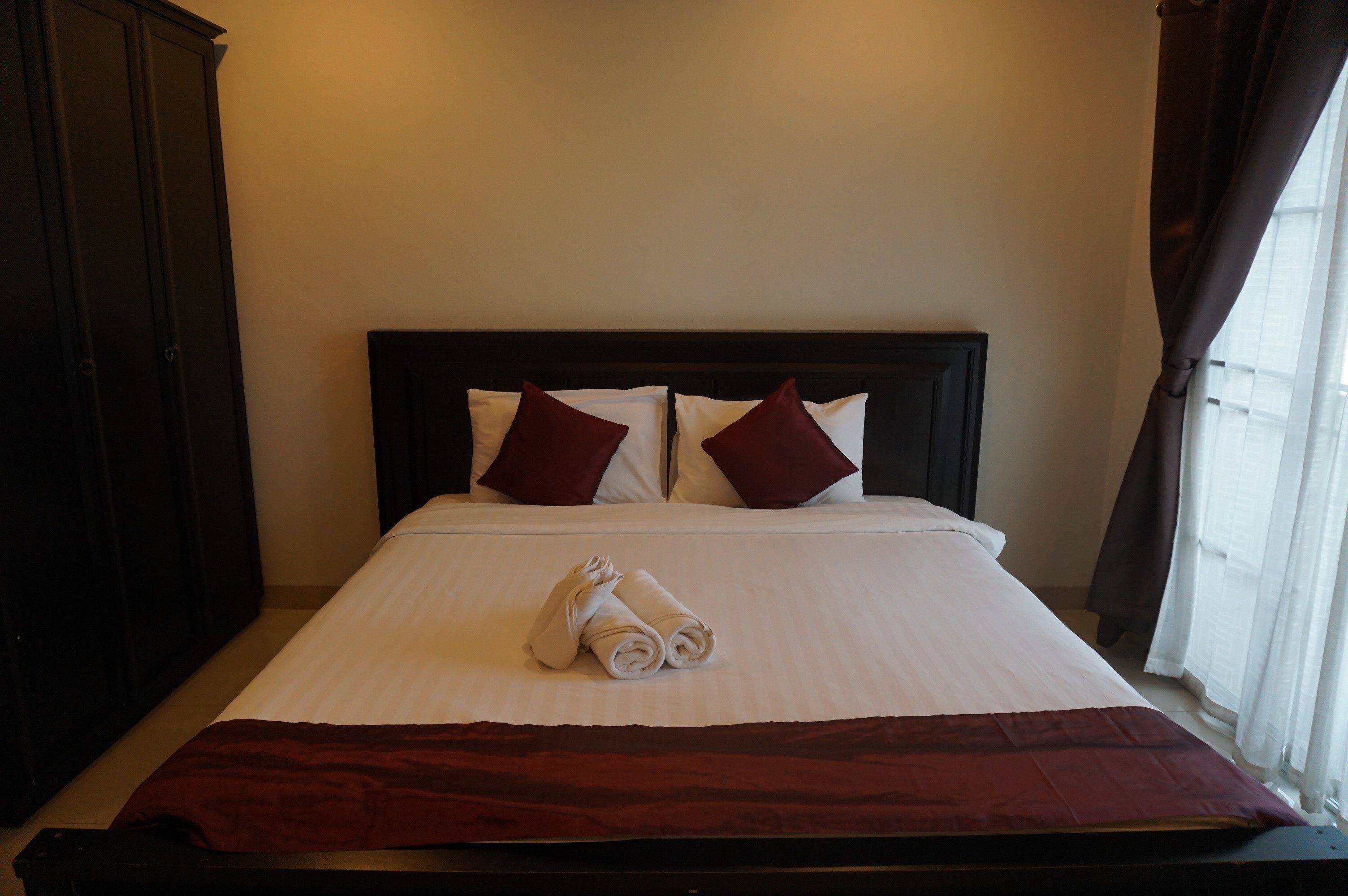 A neatly made bed with white linens and two red pillows, a dark headboard, and a red throw blanket.