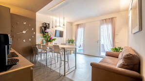 A modern living room with a sofa, a dining area with chairs, a coffee machine, and a wall clock. - Casa Ercoli (Vinci)
