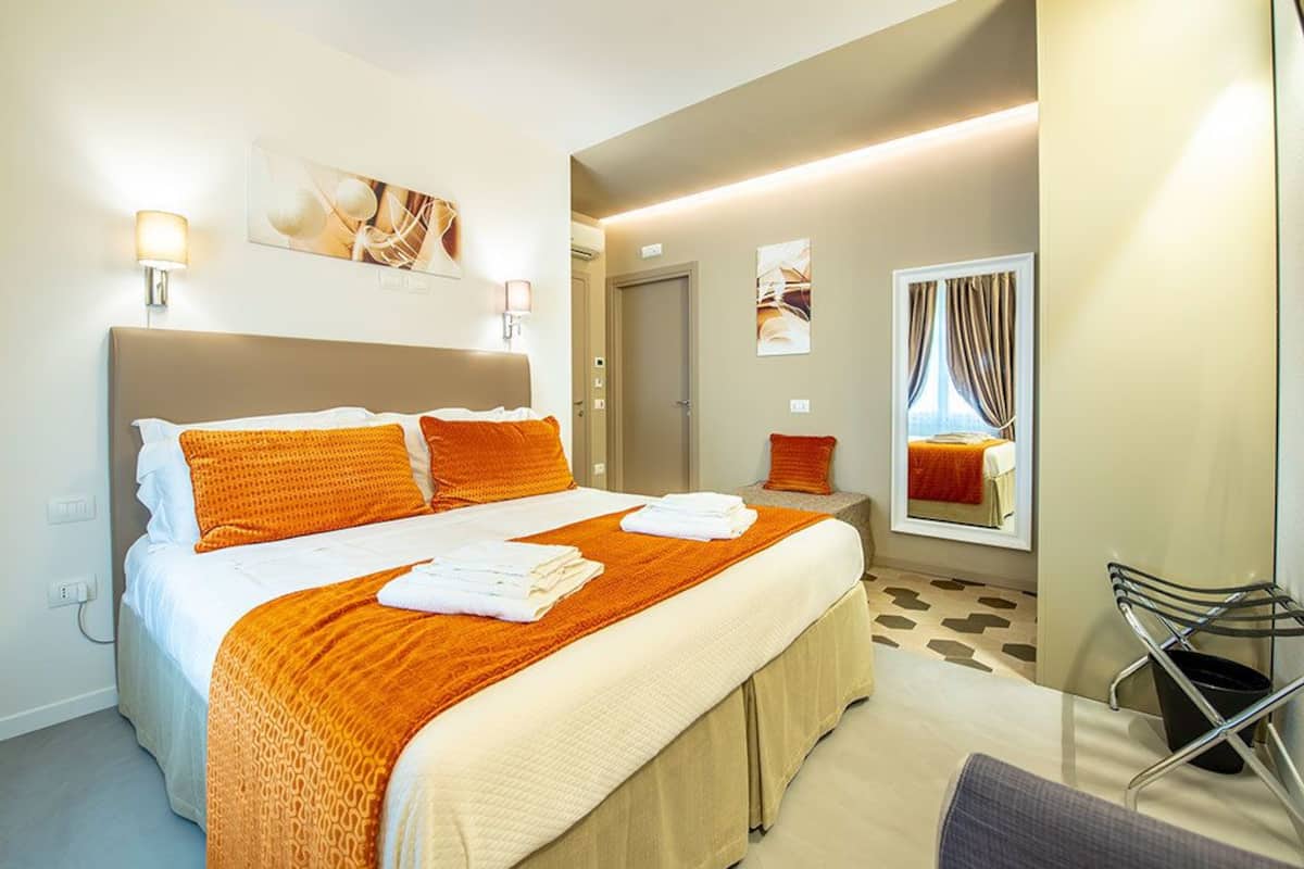 A hotel room with a large bed, two bedside tables, a chair, and a window with curtains.