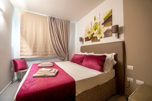 A hotel room with a bed, a window with curtains, a wall-mounted lamp, and a painting of flowers. - Casa Ercoli (Vinci)