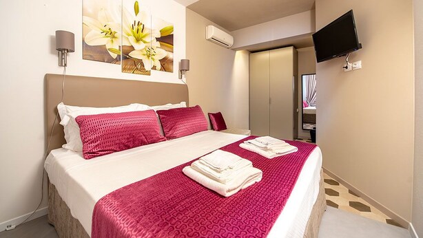 A hotel room with a bed, a flat-screen TV mounted on the wall, and a painting of flowers above the bed. - Casa Ercoli (Vinci)