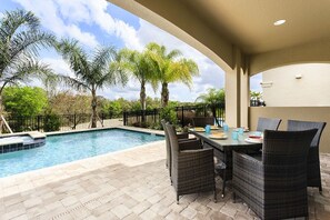 An outdoor pool area with a dining table and chairs, surrounded by palm trees and a fence. - Je59694 - Reunion Resort - 5 Bed 5 Baths Villa (Kissimmee)