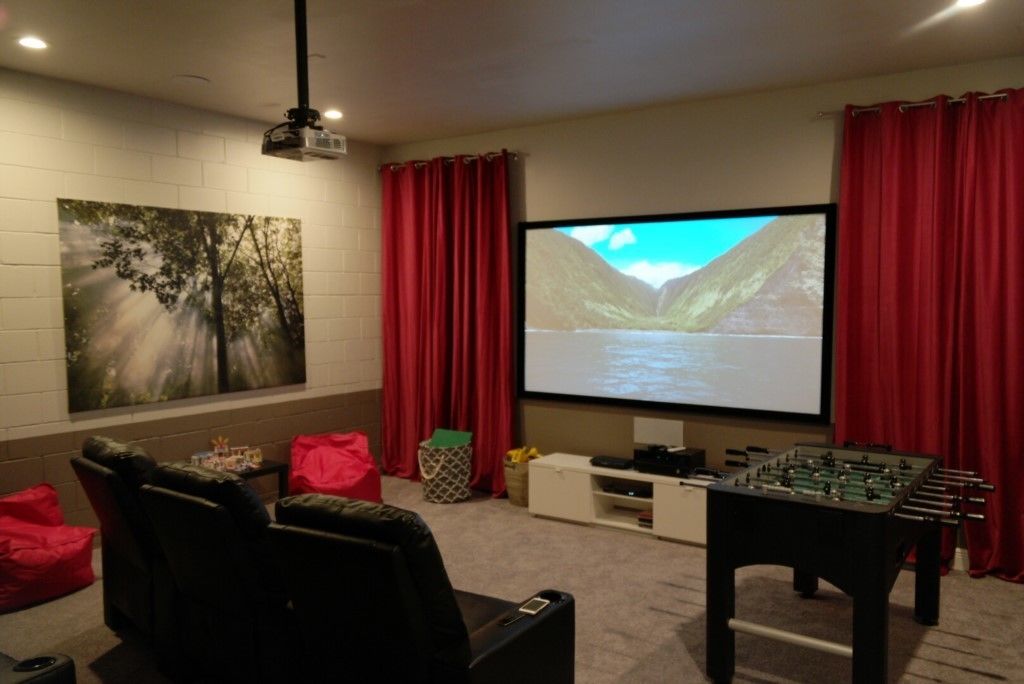 A home theater room with a large screen, red curtains, a projector, a sofa, and a foosball table.