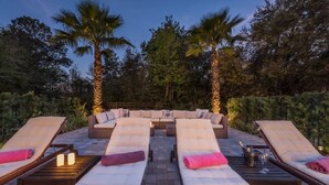 A sun lounge area with cushioned seating and a central sofa, surrounded by palm trees and a stone pathway.