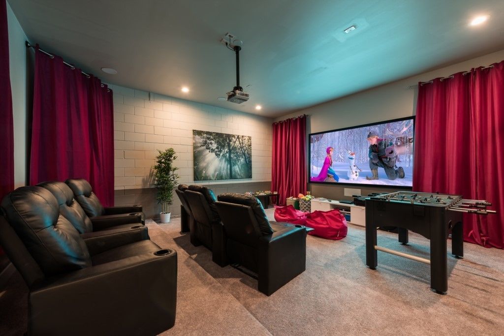 Sala de cine en casa con una pantalla grande, sillones de cuero, una mesa de fútbol de mesa y un proyector.