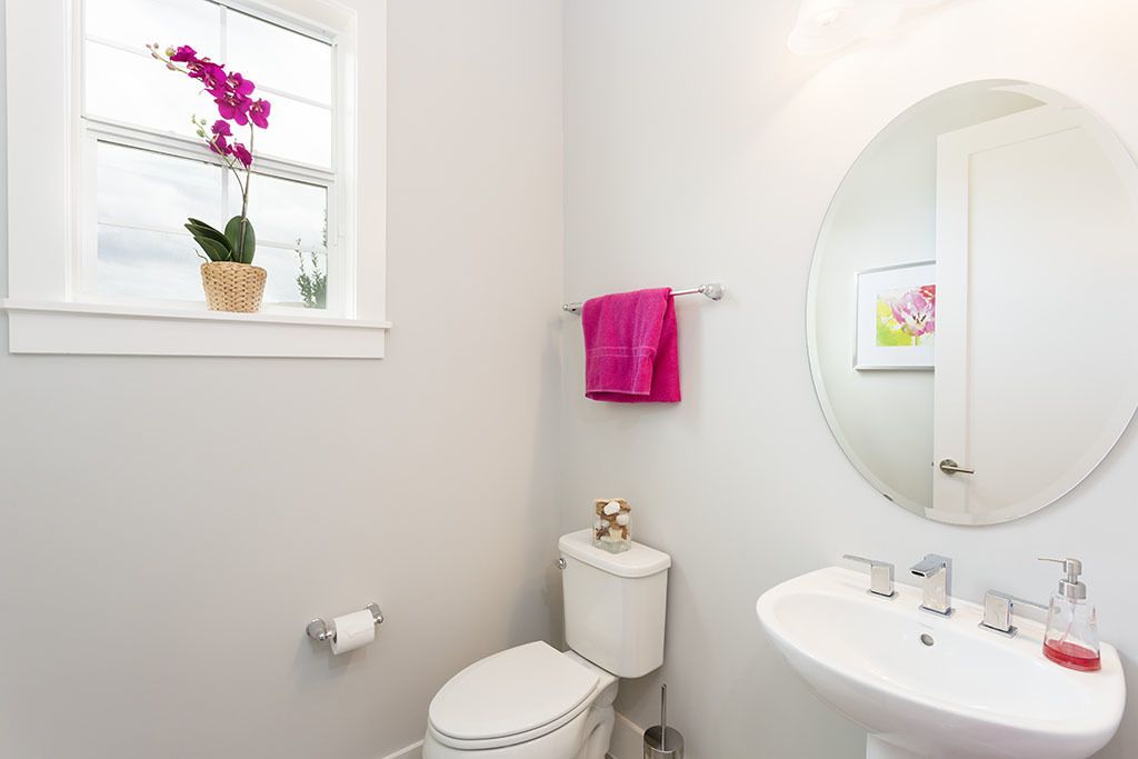 Un baño con inodoro, lavamanos y ventana con una planta de orquídea.