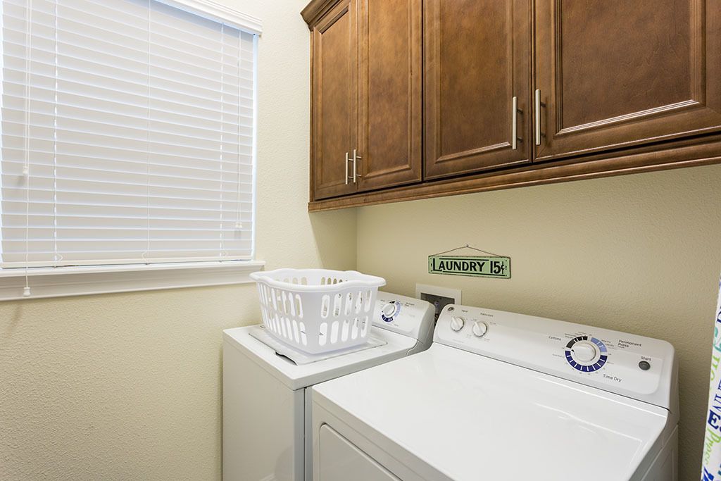 A laundry room with a white washer and dryer, wooden cabinets, a laundry basket, and a sign indicating the room's purpose.