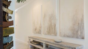 Un pasillo con un banco de madera rústica, una estantería de pared con cuencos, y un panel con varios destinos.