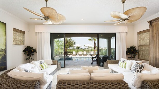 Un salón amplio con mobiliario de mimbre, piscina y grandes ventiladores de techo.