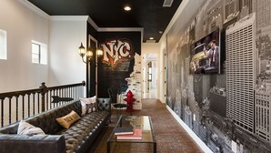 Una sala de estar acogedora con un sofá de cuero negro, una mesita de centro con libros y un mural del horizonte de Nueva York.