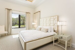 Une chambre à coucher avec un grand lit, une table de chevet avec une lampe, une chaise et une fenêtre avec des rideaux.