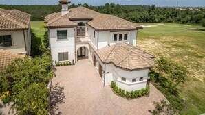 A two-story house with a tiled roof, a central entrance with a small porch, and a paved driveway. - Je61091 - Reunion Resort - 7 Bed 7 Baths Villa (Kissimmee)