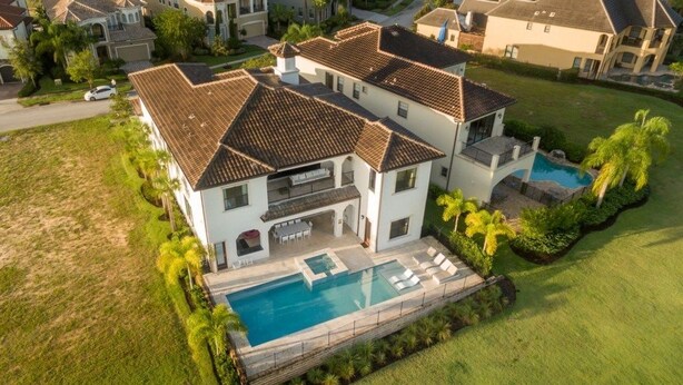 A large, two-story house with a swimming pool, surrounded by a well-maintained lawn and palm trees. - Je61091 - Reunion Resort - 7 Bed 7 Baths Villa (Kissimmee)